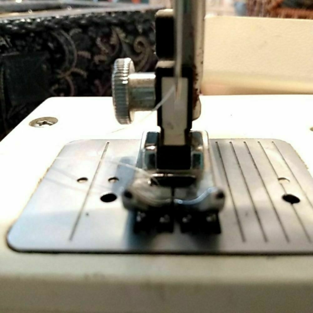 A sewing machine needle threaded with light blue thread.