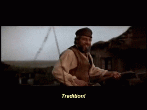 A man riding in a cart points at the sky and says "Tradition!" He's Tevye from Fiddler on the Roof.