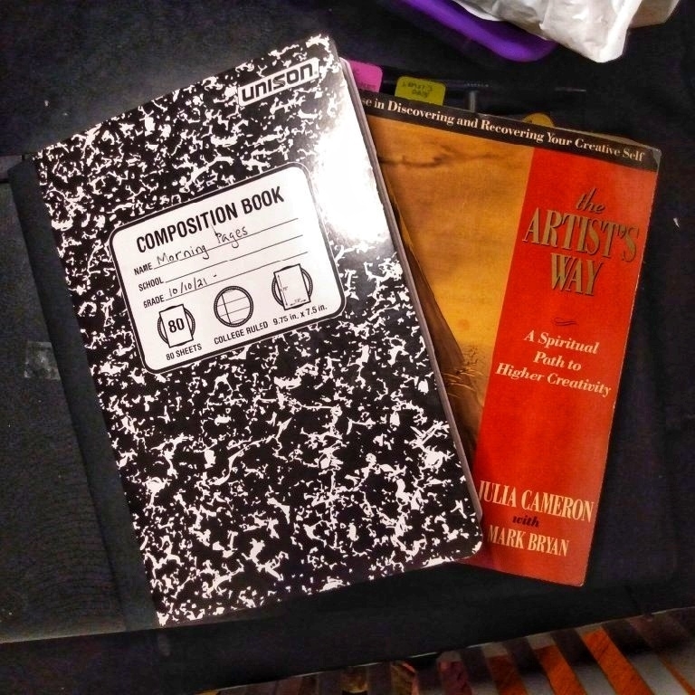 A composition notebook and a copy of the book The Artist's Way by Julia Cameron