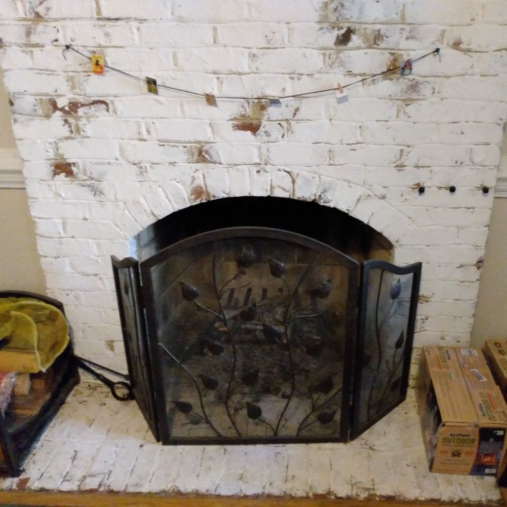 A brick fireplace, red brick painted over in places with cream paint.