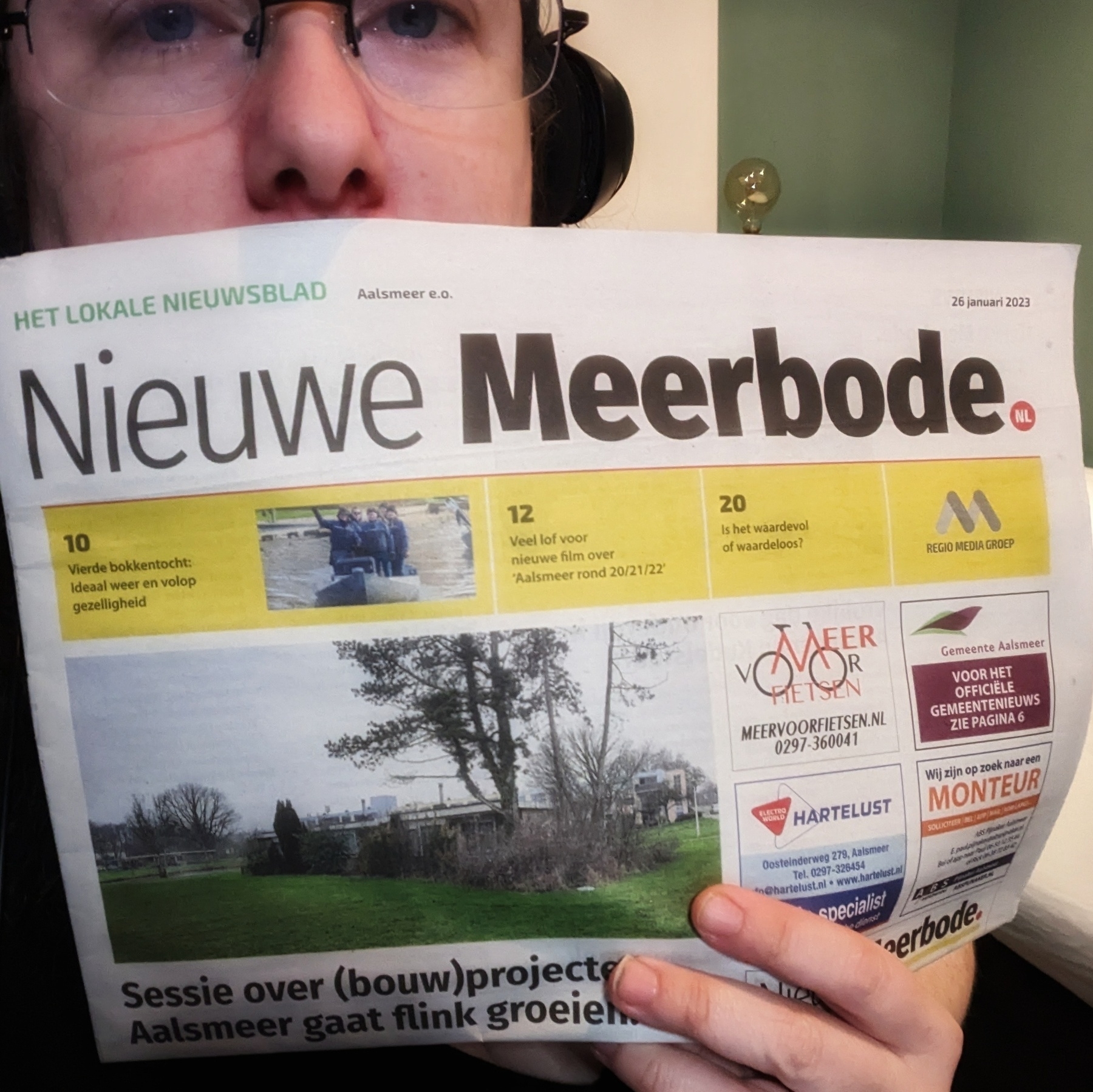 A white woman wearing glasses holds up a Dutch newspaper.