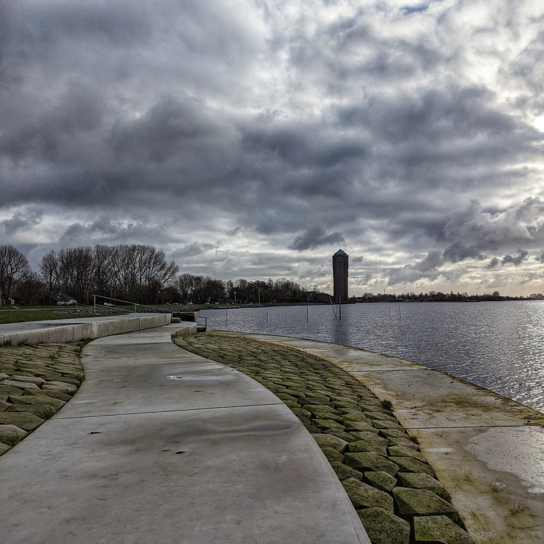 In the distance, an old brick tower looks out over a lake. In the foreground, concrete and stone steps lead down to the lake.